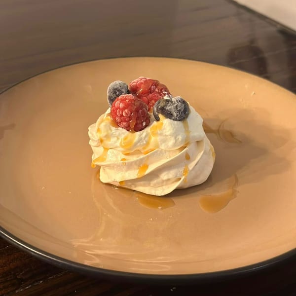 A Chai Corner meringue dessert topped with fresh raspberries, blueberries, and a caramel drizzle.