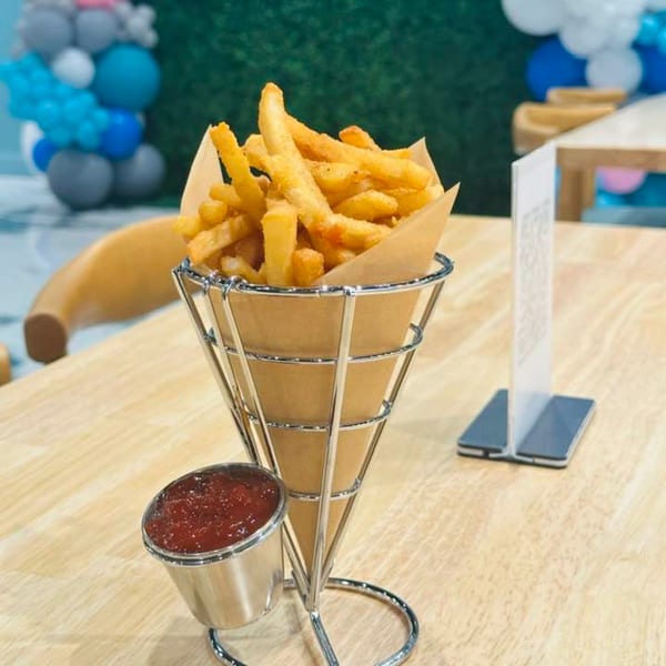 Crispy golden french fries in a metal cone holder with a side of ketchup on a wooden table.