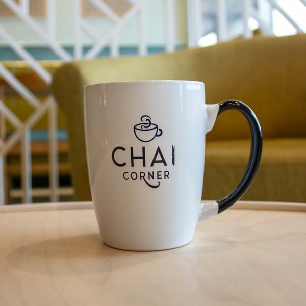 White Chai Corner mug with a black handle on a light wooden table, with a blurred background.