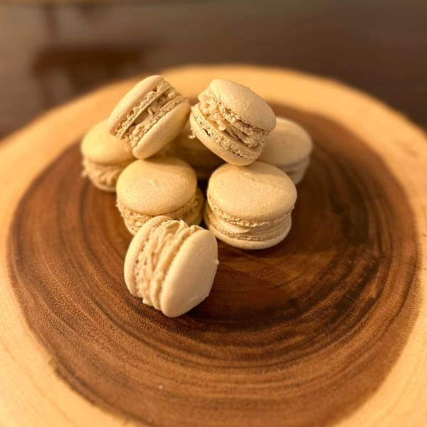 A pile of light brown macarons with creamy filling on a round wooden board.