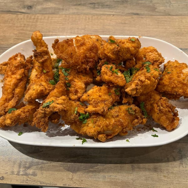 Crispy, golden-brown fried chicken pieces, garnished with fresh herbs, on a white oval plate.