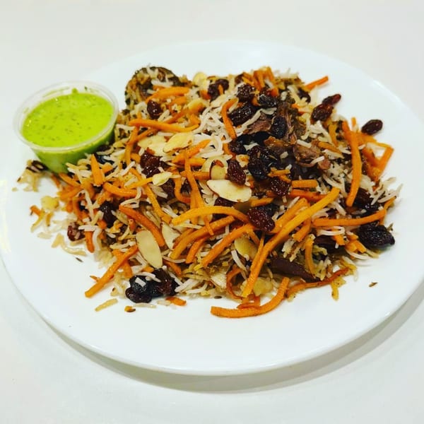 Chai Corner's Indian rice dish with carrots, raisins, almonds, and a side of green sauce.